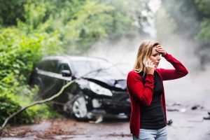 a young woman with smartphone by the damaged car