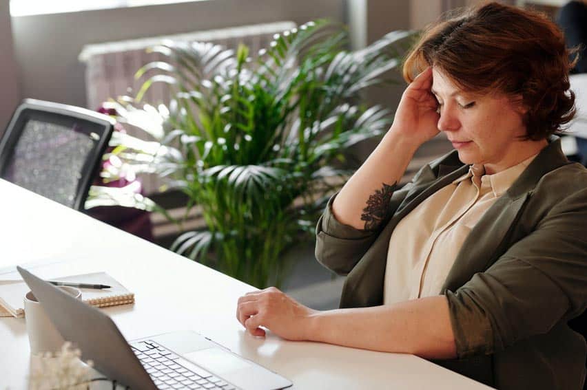 Woman massaging temple to alleviate headache at work.