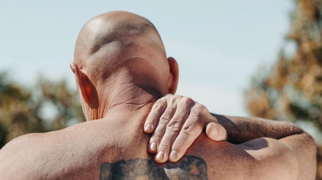 Man receiving neck and shoulder physiotherapy outdoors